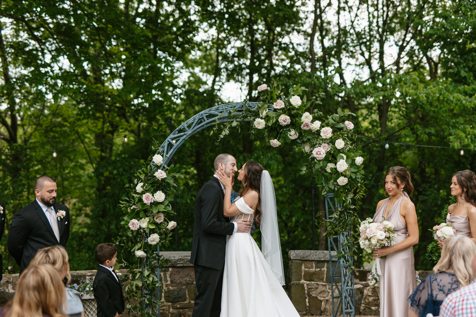 Bride and groom sharing a kiss under a floral ceremony arch