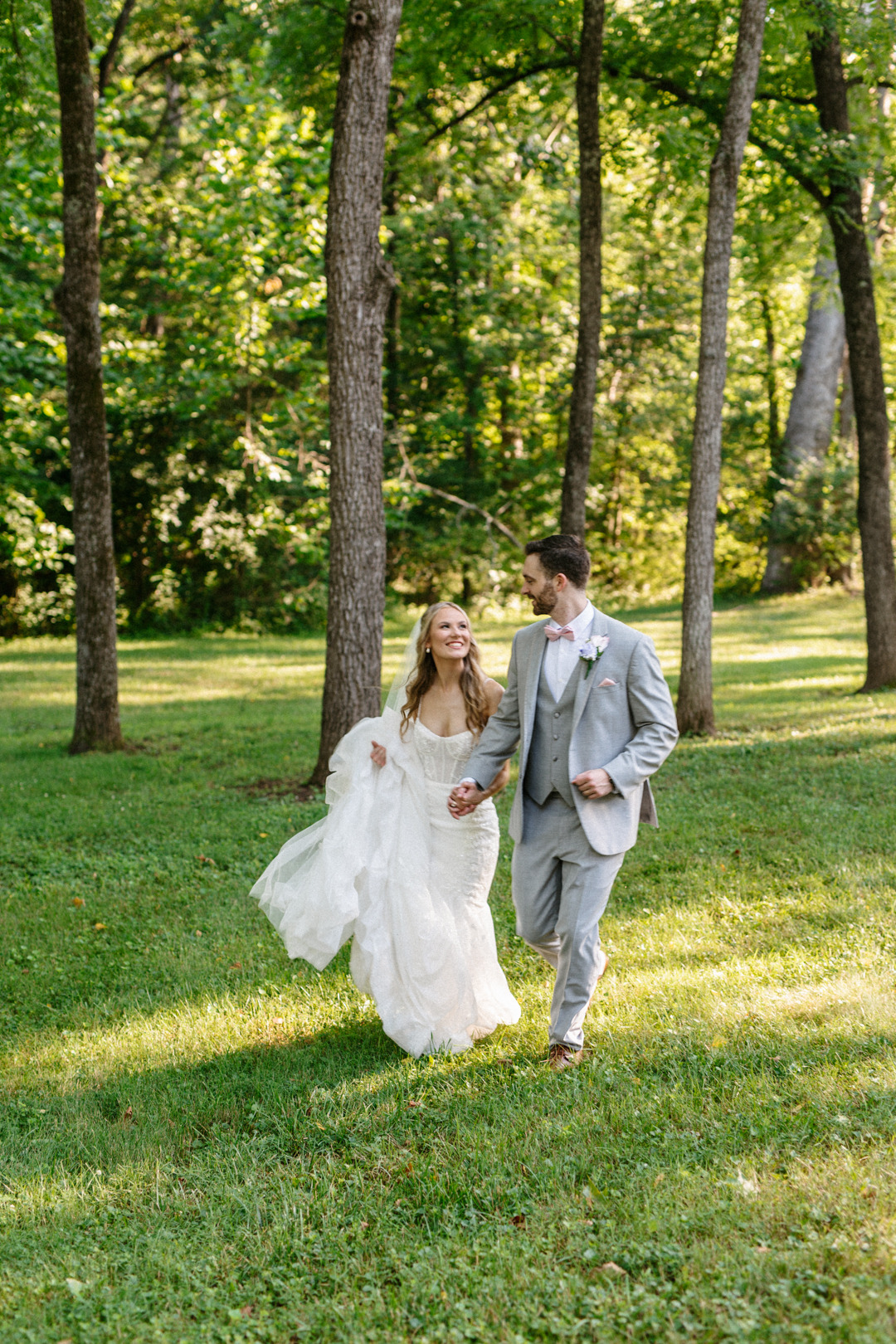 Bride and groom walking hand in hand through a sunlit wooded clearing